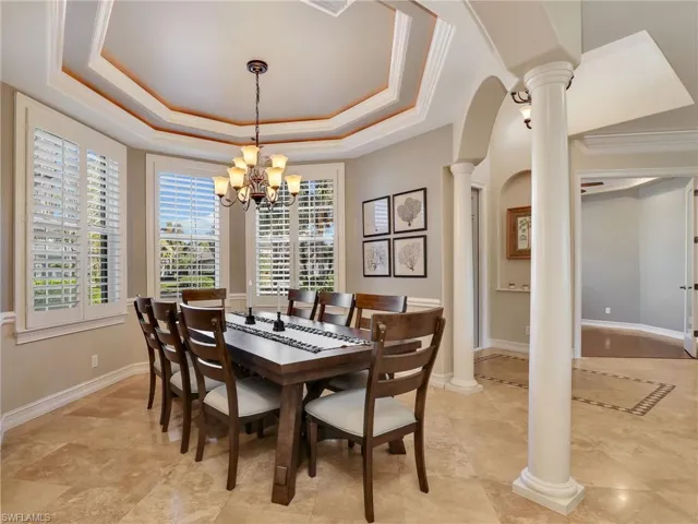 Dining room with decorative columns, crown molding, a raised ceiling, and a notable chandelier