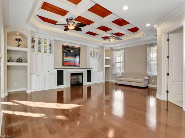 Unfurnished living room featuring ceiling fan, beamed ceiling, coffered ceiling, ornamental molding, and built in shelves