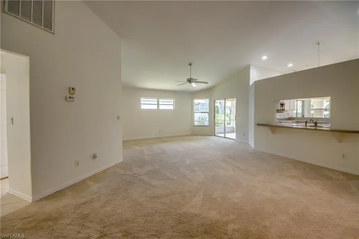 Unfurnished living room with ceiling fan, light colored carpet, high vaulted ceiling, and plenty of natural light