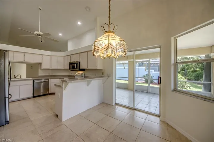 Kitchen featuring light tile patterned flooring, ceiling fan, stainless steel appliances, high vaulted ceiling, and kitchen peninsula
