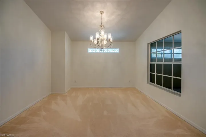 Carpeted spare room with vaulted ceiling and a chandelier