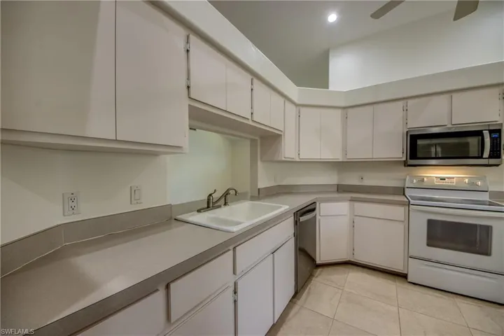 Kitchen with light tile patterned floors, white cabinets, ceiling fan, appliances with stainless steel finishes, and sink