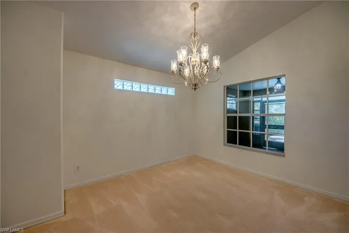 Carpeted empty room featuring a notable chandelier and lofted ceiling