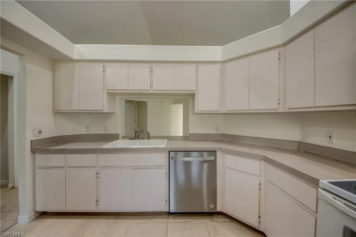 Kitchen with stainless steel dishwasher, range, white cabinets, sink, and light tile patterned floors
