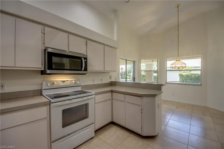 Kitchen featuring white cabinetry, white range with electric cooktop, pendant lighting, and high vaulted ceiling