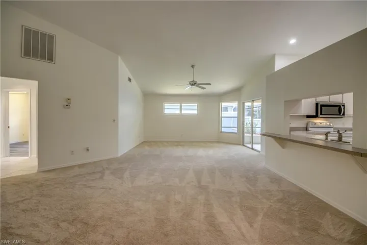 Unfurnished living room featuring sink, light carpet, ceiling fan, and vaulted ceiling