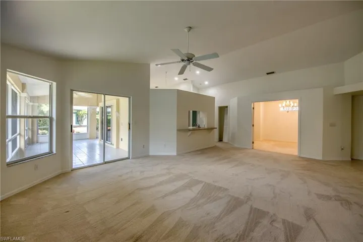 Unfurnished living room featuring light carpet, ceiling fan, and vaulted ceiling