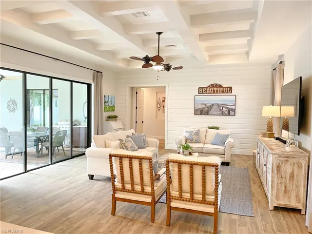 Living room with light wood-type flooring, coffered ceiling, ceiling fan, wooden walls, and beam ceiling