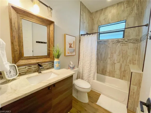 Full guest bathroom in main house with vanity, decorative backsplash, toilet, shower / tub combo with curtain, and wood-type flooring