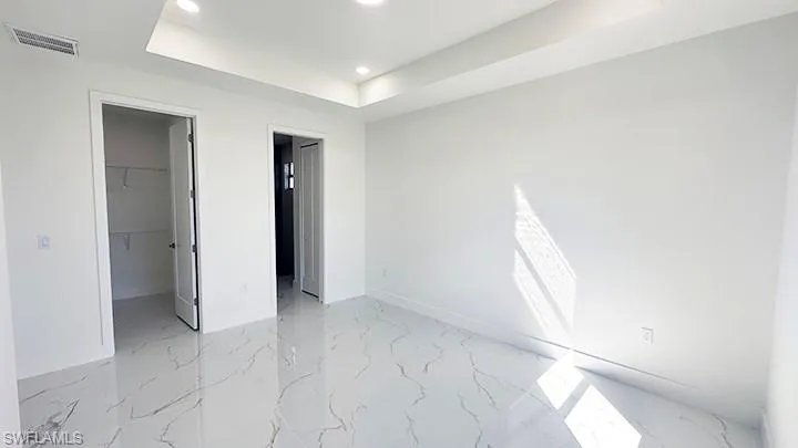 Unfurnished bedroom with a raised ceiling, a walk in closet, light marble finish floors, and recessed lighting