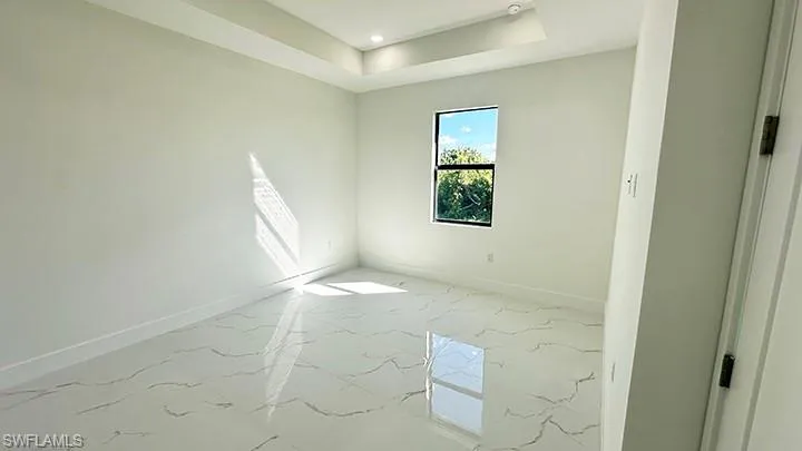 Empty room featuring light marble finish floors, recessed lighting, and a raised ceiling