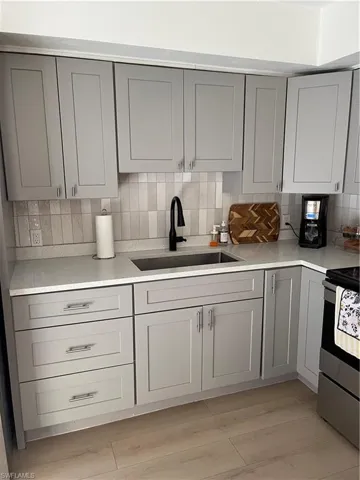 Kitchen with backsplash, light hardwood / wood-style floors, sink, gray cabinets, and stove