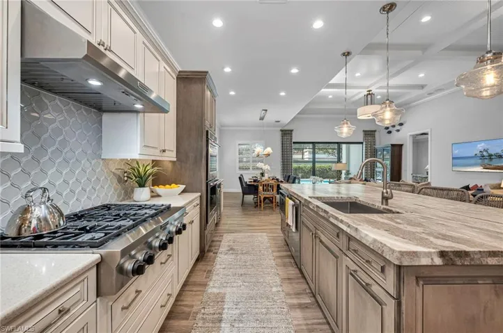 Kitchen with island with farm sink, wood look porcelain flooring, backsplash, Currey & Co light fixtures, and deep sink