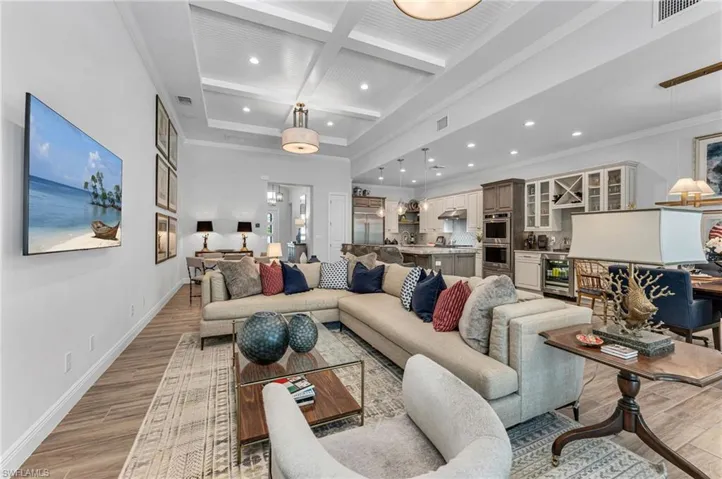 Living room featuring coffered ceiling, light hardwood / wood-style flooring, wine cooler, ornamental molding, and beamed ceiling
