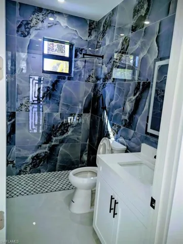 Bathroom featuring tile walls, vanity, a marble finish shower, and tile patterned floors