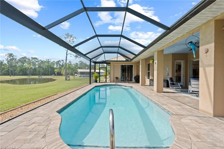 Outdoor pool featuring a water view, a yard, glass enclosure, and a patio