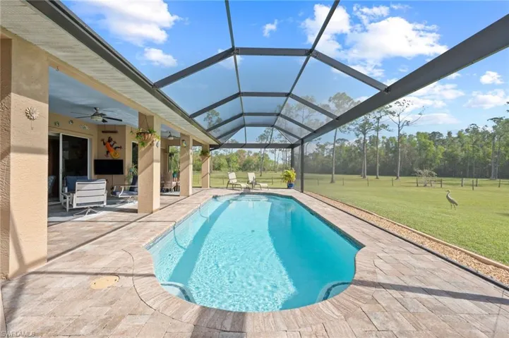 Outdoor pool featuring a ceiling fan, glass enclosure, a patio area, and a yard