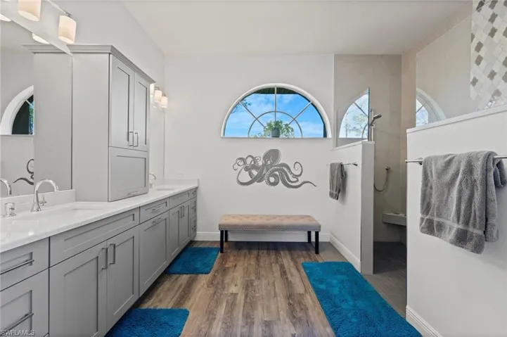Bathroom with wood finished floors, double vanity, a sink, and a walk in shower
