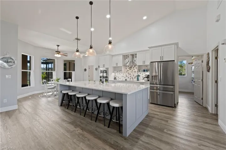Kitchen featuring a large island with sink, a breakfast bar area, stainless steel fridge with ice dispenser, plenty of natural light, and wall chimney exhaust hood