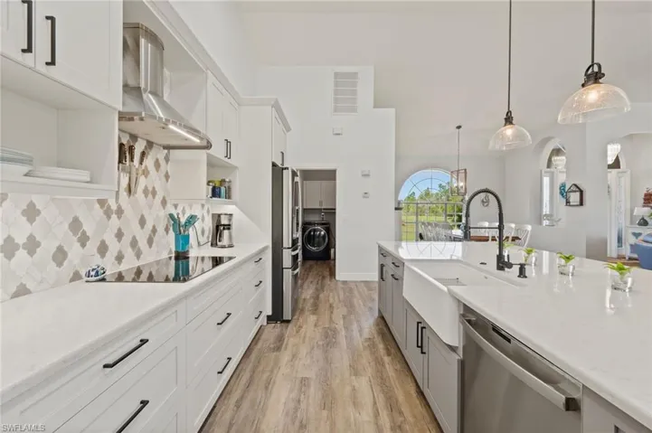 Kitchen featuring wall chimney exhaust hood, separate washer and dryer, stainless steel appliances, open shelves, and a sink