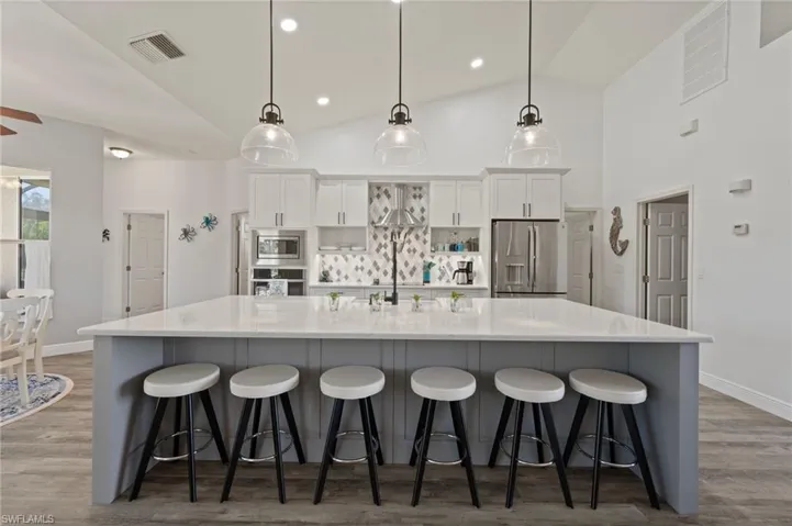 Kitchen featuring a spacious island, visible vents, appliances with stainless steel finishes, white cabinets, and a kitchen breakfast bar