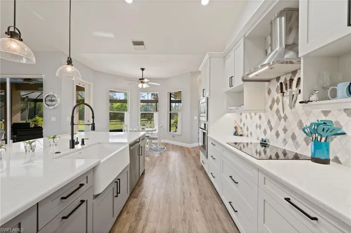 Kitchen with appliances with stainless steel finishes, decorative light fixtures, a sink, wall chimney range hood, and backsplash