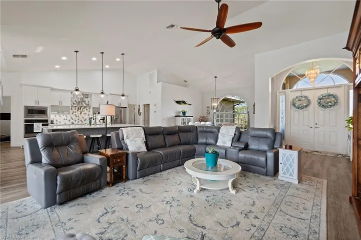 Living room featuring light wood-style floors, visible vents, high vaulted ceiling, and ceiling fan with notable chandelier