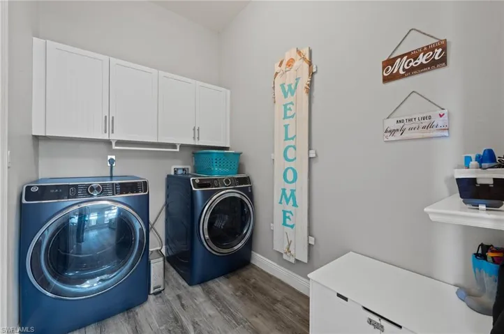 Washroom with wood finished floors, washing machine and dryer, cabinet space, and baseboards