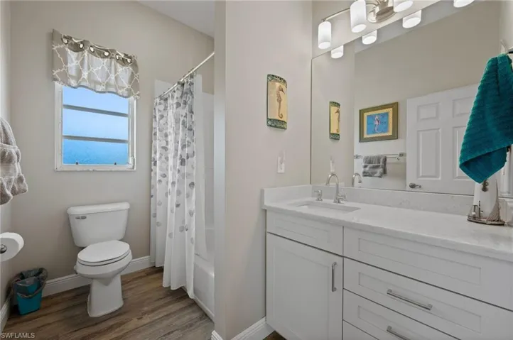 Full bath with toilet, shower / bath combo with shower curtain, vanity, wood finished floors, and baseboards
