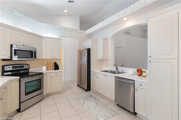 Kitchen featuring appliances with stainless steel finishes, vaulted ceiling, sink, light tile patterned floors, and white cabinetry