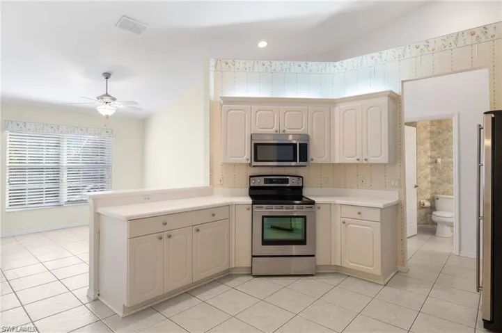 Kitchen with light tile patterned flooring, appliances with stainless steel finishes, kitchen peninsula, and ceiling fan