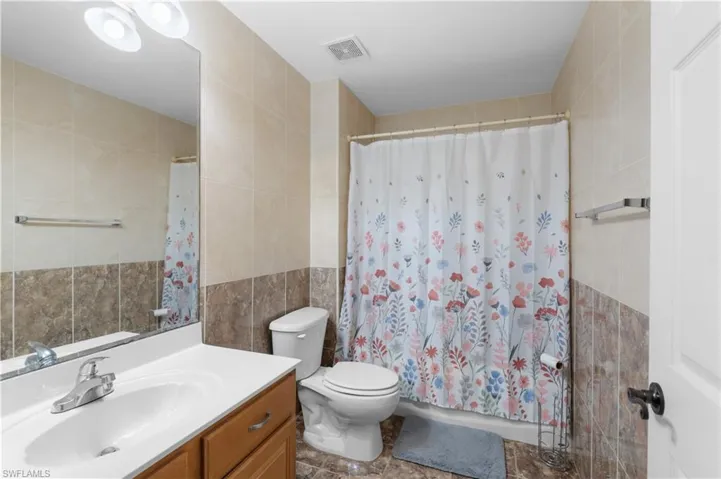 Bathroom featuring walk in shower, vanity, toilet, and tile walls