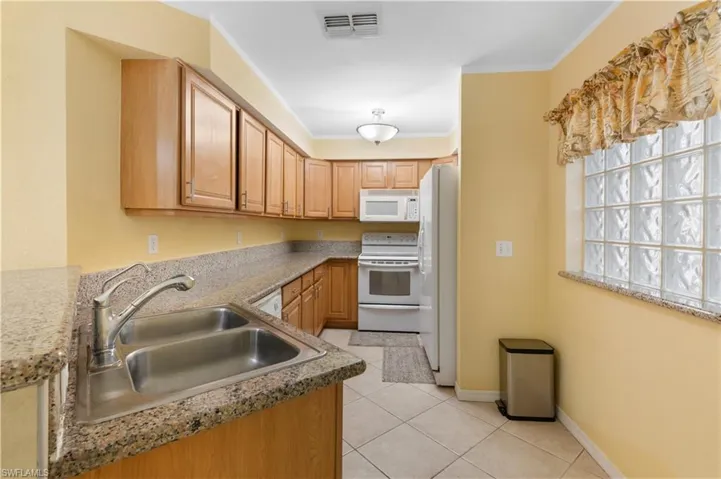 Kitchen with light tile patterned floors, white appliances, ornamental molding, and sink