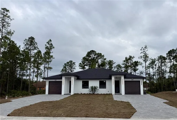 View of front of home featuring a garage, stucco siding, decorative driveway, and a front yard