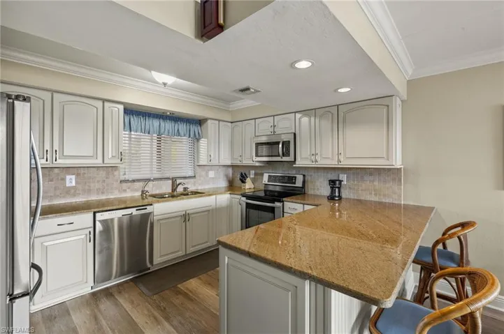 Kitchen with appliances with stainless steel finishes, white cabinetry, sink, a kitchen breakfast bar, and kitchen peninsula