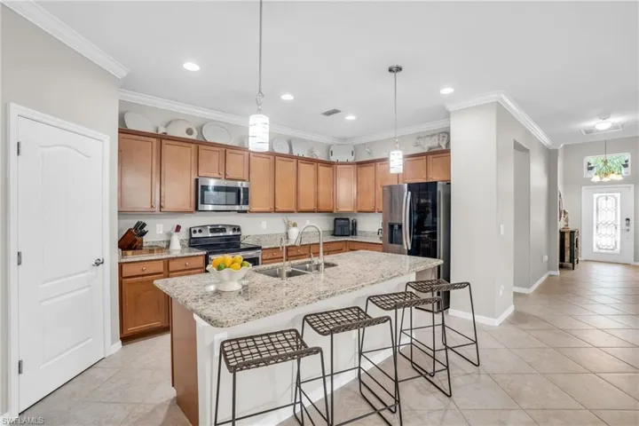 Kitchen with stainless steel appliances, pendant lighting, light tile floors, sink, and a kitchen island with sink