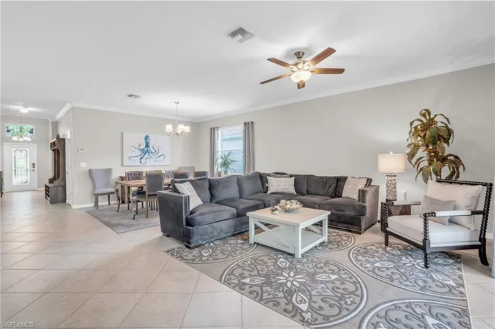 Living room featuring ornamental molding, light tile floors, and ceiling fan with notable chandelier
