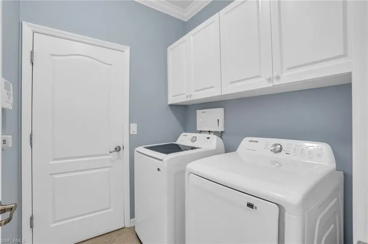 Clothes washing area featuring separate washer and dryer, ornamental molding, cabinets, and light tile floors
