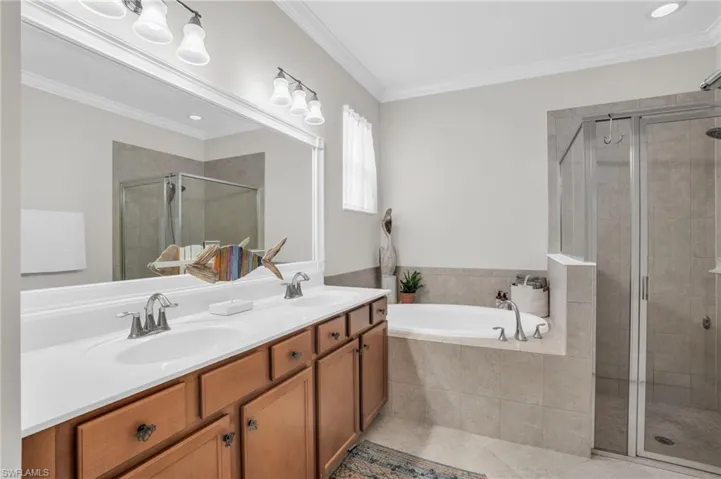 Bathroom with crown molding, tile flooring, shower with separate bathtub, and dual bowl vanity