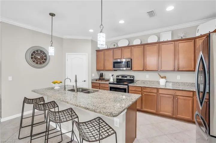 Kitchen featuring decorative light fixtures, an island with sink, ornamental molding, appliances with stainless steel finishes, and sink