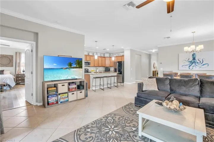 Tiled living room featuring ornamental molding and ceiling fan with notable chandelier
