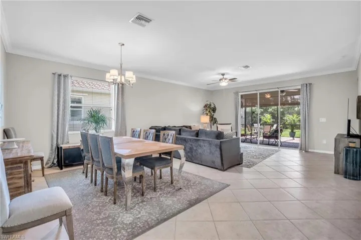 Tiled dining room with ceiling fan with notable chandelier and crown molding