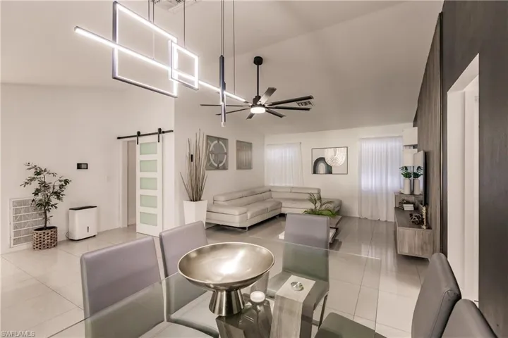 Living room with lofted ceiling, a barn door, light tile patterned floors, and ceiling fan