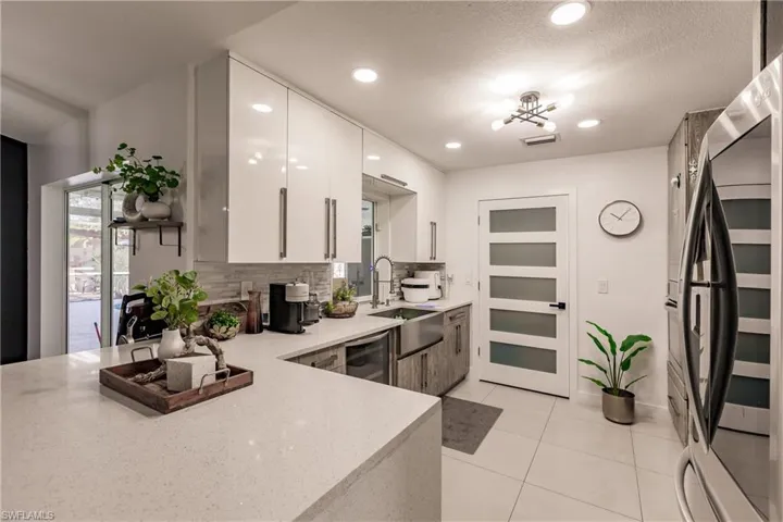 Kitchen with backsplash, sink, light tile patterned floors, white cabinetry, and stainless steel refrigerator