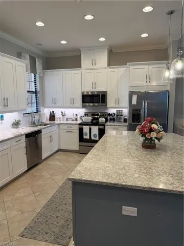 Kitchen featuring stainless steel appliances, ornamental molding, light stone countertops, white cabinetry, and pendant lighting