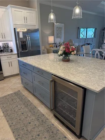 Kitchen featuring wine cooler, two tone cabinetry, light stone countertops, fridge, and crown molding