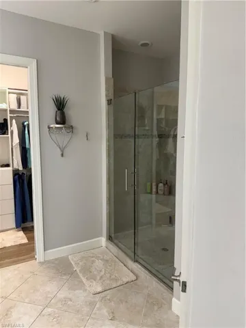 Full bathroom featuring a stall shower, a spacious closet, and light tile patterned flooring