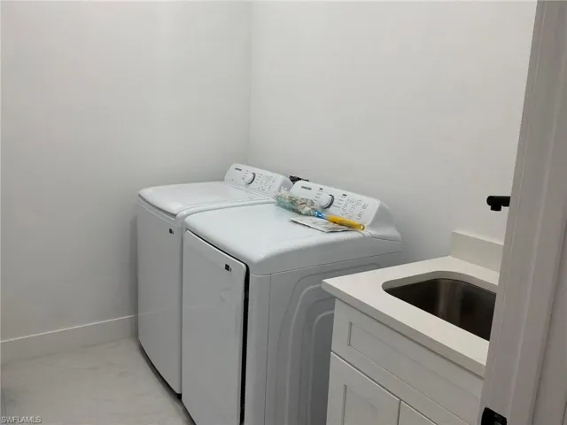Dedicated laundry area featuring a utility sink with a stone-finish countertop, white cabinetry, and white flooring