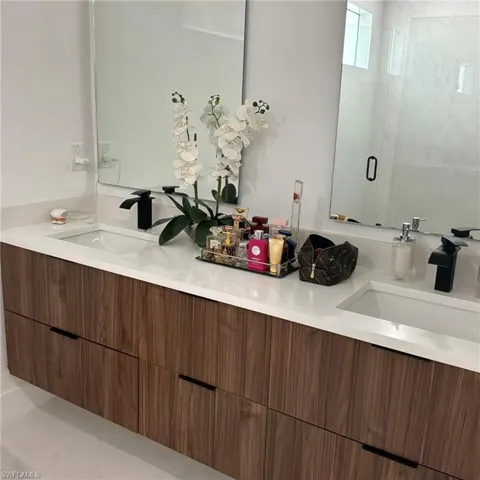 Dual vanity with a wood-finish floating cabinet, white countertop, integrated sinks, and matte black faucets