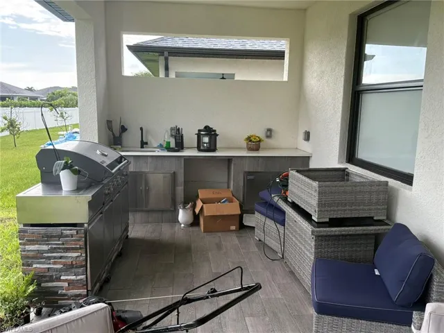 Covered outdoor kitchen featuring a built-in grill, integrated sink, and stone-finish accents